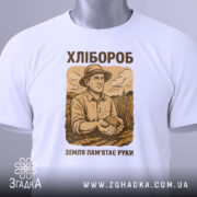 Футболка з малюнком хлібороба, білого кольору, зображена з фронтального ракурсу на манекені, фон світло-сірий, принт з малюнком хлібороба в капелюсі, що тримає в руках землю, текст "ХЛІБОРОб" та "ЗЕМЛЯ ПАМ'ЯТАЄ РУКИ" в коричневих тонах.