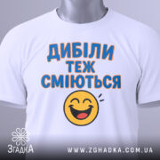 Футболка з написом Дибіли, білого кольору, з фронтального ракурсу, на манекені, фон нейтральний, принт з текстом "Дибіли теж сміються" та смайлом.