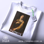 Футболка з написом PYZDETS, білого кольору, лежить на поверхні, фон світлий, принт зображає жінку в історичному костюмі, що дивиться вгору, з червоним плащем, на комірці є етикетка.