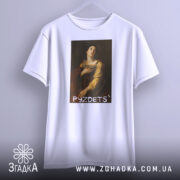 Футболка з написом PYZDETS, білого кольору, підвішена на вішалці, фон нейтральний, принт зображає жінку в історичному костюмі, що дивиться вгору, з червоним плащем.