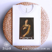 Футболка з написом PYZDETS, білого кольору, складена на кошику, фон світлий, принт зображає жінку в історичному костюмі, що дивиться вгору, з червоним плащем.