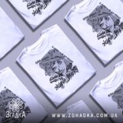 Футболка з написом свободи, білого кольору, розкладена на плоскій поверхні, фон світло-сірий, кілька футболок з принтом зображують жінку з літаками та текстами, вид зверху.