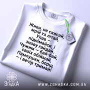 Футболка з поетичним текстом, білого кольору, зображена зверху, з видимим етикеткою зеленого кольору, фон світло-сірий, текст чорного кольору, розташований по центру, з чіткими рядками.