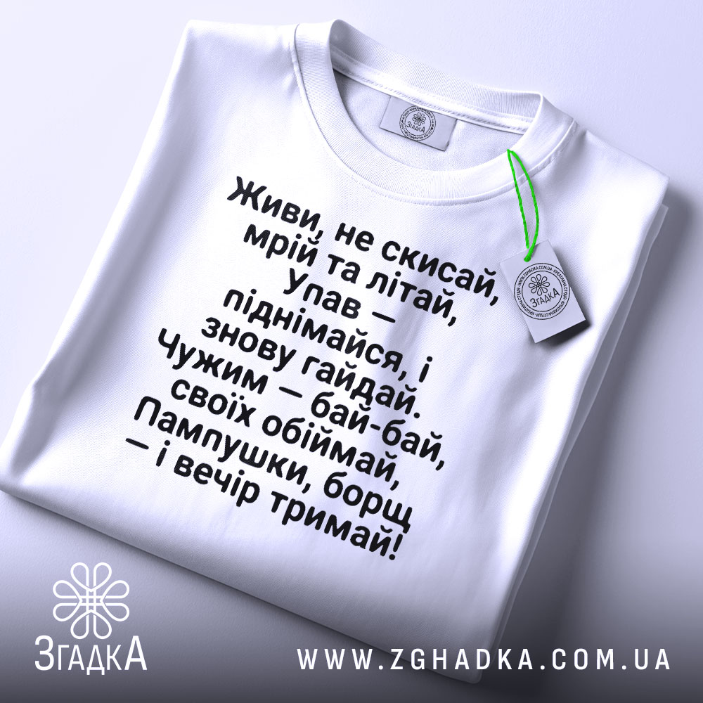 Футболка з поетичним текстом, білого кольору, зображена зверху, з видимим етикеткою зеленого кольору, фон світло-сірий, текст чорного кольору, розташований по центру, з чіткими рядками.