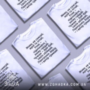 Футболка з поетичним текстом, білого кольору, зображена зверху на кількох складених футболках, фон світло-сірий, текст чорного кольору, розташований по центру, з чіткими рядками.