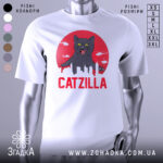 Футболка з принтом Catzilla білого кольору, зображена з фронтального ракурсу на манекені, фон світло-сірий, принт містить чорного кота на червоному фоні з силуетами міста та вертольотами.
