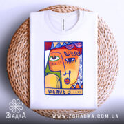 Футболка з текстом beauty, білого кольору, зображена зверху на плетеному кошику, фон світлий, принт з абстрактним обличчям в яскравих кольорах.