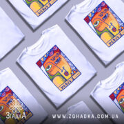 Футболка з текстом beauty, білого кольору, зображена на столі, фон світло-сірий, кілька футболок з принтом з абстрактним обличчям в яскравих кольорах, складені разом.