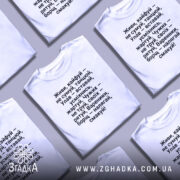 Футболка живи кайфуй не сумуй. Біла футболка, розкладена на поверхні, з текстом чорного кольору. Фон світло-сірий, акцент на тексті.