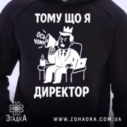Худі я директор подарунок. Чорний колір, ракурс з близької відстані, фон світлий. Принт з малюнком директора, який тримає мегафон, текст "ТОМУ ЩО Я ДИРЕКТОР". Капюшон видимий, манжети з еластичної тканини.