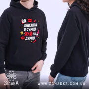 Худі книжка в сумці, темно-синього кольору, з капюшоном, з кишенею-«кенгуру», на фоні видно двох людей, які його носять. Принт на грудях яскравий, з елементами червоного, жовтого та чорного кольорів, текст українською мовою.