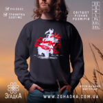 Світшот дика енергія подарунок, чорний колір, зображення моделі в природному фоні на заході сонця, принт з білим ведмедем та червоними елементами, кругла горловина, манжети з трикотажної резинки, пояс з трикотажної резинки, фактура м'яка та приємна на дотик.