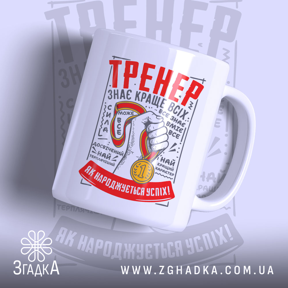 Чашка для найкращого тренера, біла, зображена в ракурсі з правого боку, на фоні світло-сірого кольору. Принт містить червоний напис 'ТРЕНЕР' та зображення руки з медаллю. Ручка кругла, край чашки гладкий, поверхня матова.