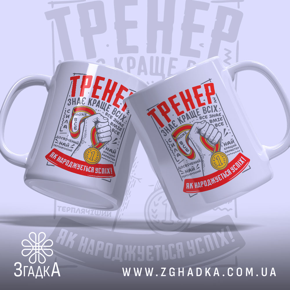 Чашка для найкращого тренера, біла, зображена в ракурсі з двох боків, на фоні світло-сірого кольору. Принт містить червоний напис 'ТРЕНЕР' та зображення руки з медаллю. Ручки чашок круглі, краї гладкі, поверхня матова.