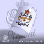 Чашка для прекрасної королеви. Чашка білого кольору з чорним і золотим принтом. Ракурс зліва, фон світло-фіолетовий з елементами корони. Ручка класичної форми, край гладкий, поверхня глянцева.