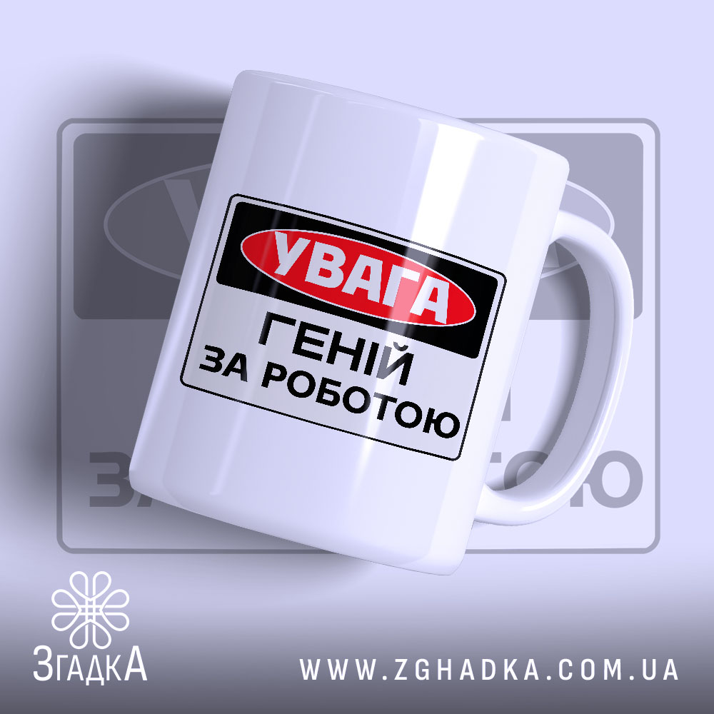 Chashka Henii Za Robotoiu Idealnyi Podarunok Dlia Kreatyvnykh 1 Чашка геній за роботою. Чашка білого кольору з чорним і червоним принтом, на якому написано 'УВАГА ГЕНІЙ ЗА РОБОТОЮ'. Ручка гладка, край рівний, поверхня має легкий глянець. Фон світло-фіолетовий, з розмитим логотипом.