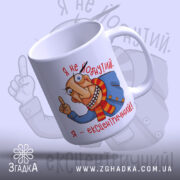 Чашка я ексцентричний, біла з кольоровим малюнком, показує персонажа з великими очима, що вказує пальцем, ручка з правого боку, край гладкий, глянцевий фініш.