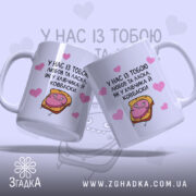 Чашка хлібчик й ковбаска, дві білих чашки з кольоровим принтом, показані з легким нахилом, на фоні світло-фіолетового кольору з сердечками, з малюнком хлібчика і ковбаски, ручки класичні, краї рівні, глянцева поверхня.