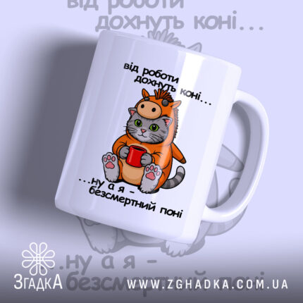 Чашка коні поні. Чашка білого кольору з малюнком кота в костюмі поні, що тримає червону чашку. Ручка чашки з правого боку, край рівний, поверхня глянцева. На фоні розмитий малюнок з написом.