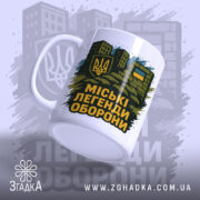 Чашка міські легенди оборони, біла, зображена з правого ракурсу, на фоні стилізованих будівель, принт з гербом України та написом на чорному фоні, ручка класична, край рівний, глянцевий.