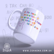 Чашка на річницю зустрічі, біла, з кольоровим принтом, на якому написано: 'Я ТАК СИЛЬНО ЛЮБЛЮ ТЕБЕ!' та малюнок зайця. Ручка кругла, край гладкий, глянець на поверхні чашки, фон світло-фіолетовий.