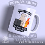 Чашка нахабний кіт, біла з кольоровим принтом, зображення нахабного кота з комп'ютером на чорному фоні, ручка з правого боку, край рівний, матова поверхня.