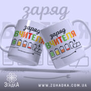 Чашка рівень заряду вчителя. Білий фон, ракурс з двох чашок, що стоять поруч, кольоровий принт з написом "заряд вчителя" та малюнками батарейок. Ручки класичні, краї рівні, поверхня глянцева.