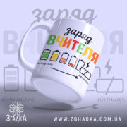 Чашка рівень заряду вчителя. Білий фон, ракурс зліва, на чашці кольоровий принт з написом "заряд вчителя" та малюнками батарейок. Ручка класична, край рівний, поверхня глянцева.