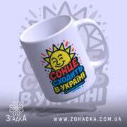 Чашка сонце в Україні, біла, з ракурсом зліва, на фоні світло-фіолетового кольору, з яскравим принтом сонця та написом 'СОНЦЕ СХОДИТЬ В УКРАЇНІ', ручка гладка, край рівний, глянцевий.