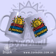 Чашка сонце в Україні, дві білих чашки, з ракурсом спереду, на фоні світло-фіолетового кольору, з яскравим принтом сонця та написом 'СОНЦЕ СХОДИТЬ В УКРАЇНІ', ручки гладкі, краї рівні, глянцеві.
