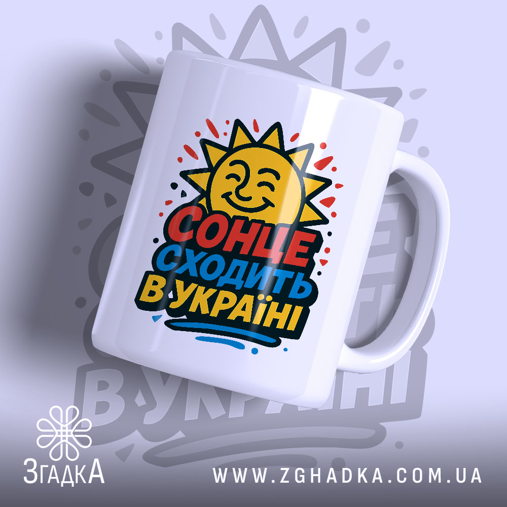 Чашка сонце в Україні, біла, з ракурсом зліва, на фоні світло-фіолетового кольору, з яскравим принтом сонця та написом 'СОНЦЕ СХОДИТЬ В УКРАЇНІ', ручка гладка, край рівний, глянцевий.