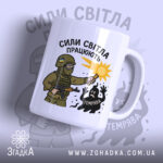 Чашка сили світла працюють, біла з малюнком, показує військового з ліхтарем, на фоні світло-сірого кольору, з написом 'СИЛИ СВІТЛА ПРАЦЮЮТЬ', ручка стандартна, край рівний, матова поверхня.