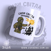 Чашка сили світла працюють, біла з малюнком, показує військового з ліхтарем, на фоні світло-сірого кольору, з написом 'СИЛИ СВІТЛА ПРАЦЮЮТЬ', ручка стандартна, край рівний, матова поверхня.