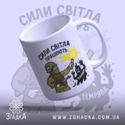 Чашка сили світла працюють, біла з малюнком, показує військового з ліхтарем, на фоні світло-сірого кольору, з написом 'СИЛИ СВІТЛА ПРАЦЮЮТЬ', ручка стандартна, край округлий, матова поверхня.