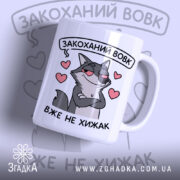 Чашка закоханий хижак, біла з малюнком сірого вовка, що має хитру усмішку, на фоні сердечок, ручка класична, край рівний, глянцевий.