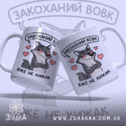 Чашка закоханий хижак, дві білі чашки з малюнком сірого вовка, що має хитру усмішку, на фоні сердечок, ручки класичні, краї рівні, глянцеві.