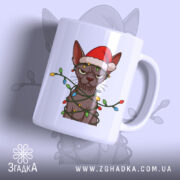 Чашка злий новорічний кіт, біла, зображення кота в червоній шапці та гірлянді, ручка з правого боку, глянець на поверхні, фон світло-сірий.