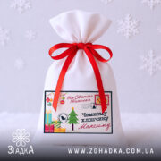 Дитячий святковий мішечок на білому фоні зі сніжинками, червоною стрічкою і новорічним принтом.