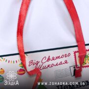 Дитячий святковий мішечок крупним планом — фрагмент із написом “Від Святого Миколая” і декоративними лампочками.
