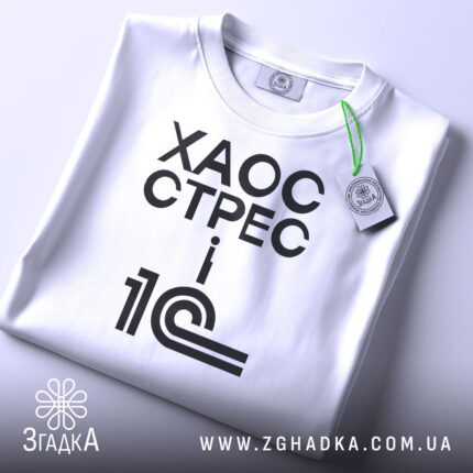 Футболка 1с хаос стрес, складена футболка на світлому фоні, ракурс зверху, принт чорний з текстом 'ХАОС СТРЕС i 1С', на комірці зелена етикетка.