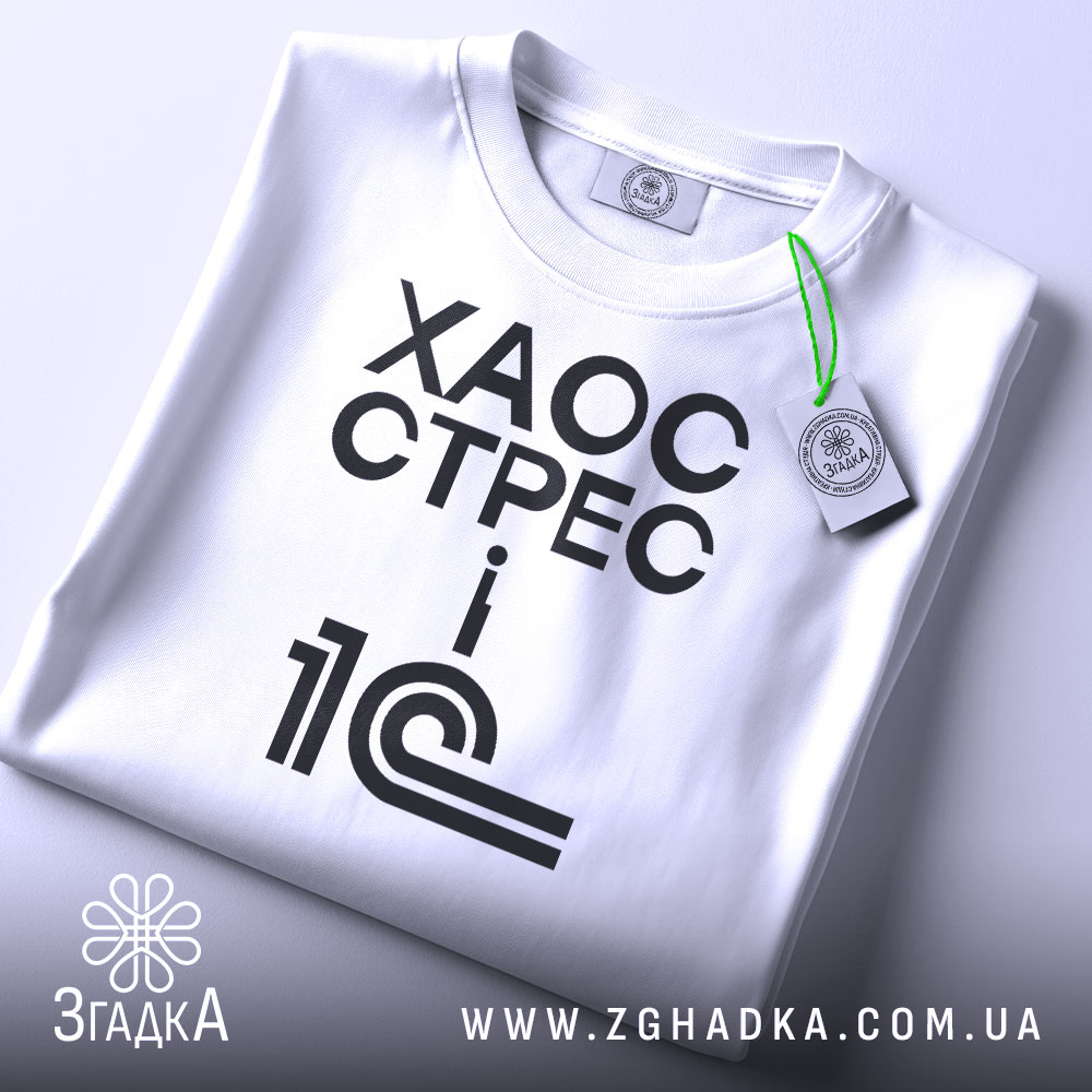 Футболка 1с хаос стрес, складена футболка на світлому фоні, ракурс зверху, принт чорний з текстом 'ХАОС СТРЕС i 1С', на комірці зелена етикетка.
