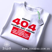 Футболка 404 human not found, біла, складена на поверхні, фон світло-сірий, принт червоний з текстом 'ERROR 404 HUMAN NOT FOUND' та 'SORRY! THE HUMAN YOU ARE LOOKING FOR DOES NOT EXIST', на комірці зелена етикетка.