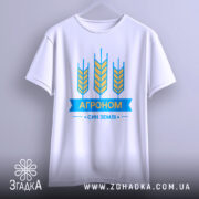 Футболка агроном син землі, біла, зображена з фронтального ракурсу на вішалці, фон градієнтний сірий, принт з жовтими колосками та синьою стрічкою з написом "АГРОНОМ".