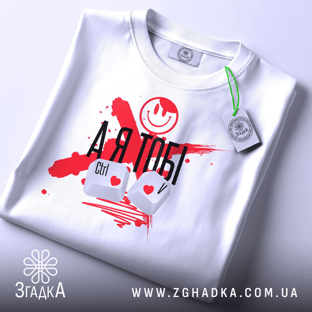Футболка айті романтика, біла, складена на поверхні, фон світло-сірий, принт з червоними плямами, смайлом та написом 'А Я ТОБІ', клавіші Ctrl і V з сердечками, на етикетці зелена стрічка.