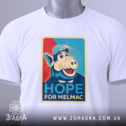 Футболка Альф білого кольору, складена на столі, ракурс зверху, фон світло-сірий, принт з персонажем свині в кепці, текст "HOPE FOR MELMAC" з елементами графіки.