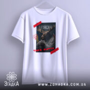 Футболка Аляска таке життя, біла футболка з принтом, зображення оленя з рогами, на фоні прапорів України та США, текст 'ТАKE ЖИТТЯ' червоним кольором, ракурс спереду на вішалці.