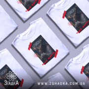 Футболка Аляска таке життя, біла футболка з принтом, зображення оленя з рогами, на фоні прапорів України та США, текст 'ТАKE ЖИТТЯ' червоним кольором, ракурс спереду.