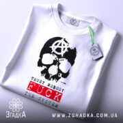 Футболка анархія проти системи, біла, зображена на столі, фон світлий, принт з черепом та анархічним символом, текст 'TRUST NOBODY FUCK THE SYSTEM' червоного кольору, на футболці є етикетка.