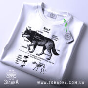 Футболка анатомія вовка, біла, зображена зверху, на фоні світлого кольору, принт чорного кольору з деталями анатомії вовка, на комірці є етикетка.