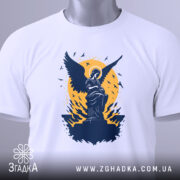 Футболка ангел України, біла, складена на столі, фон світло-сірий, принт з ангелом на фоні жовтого кола, з етикеткою зеленого кольору.